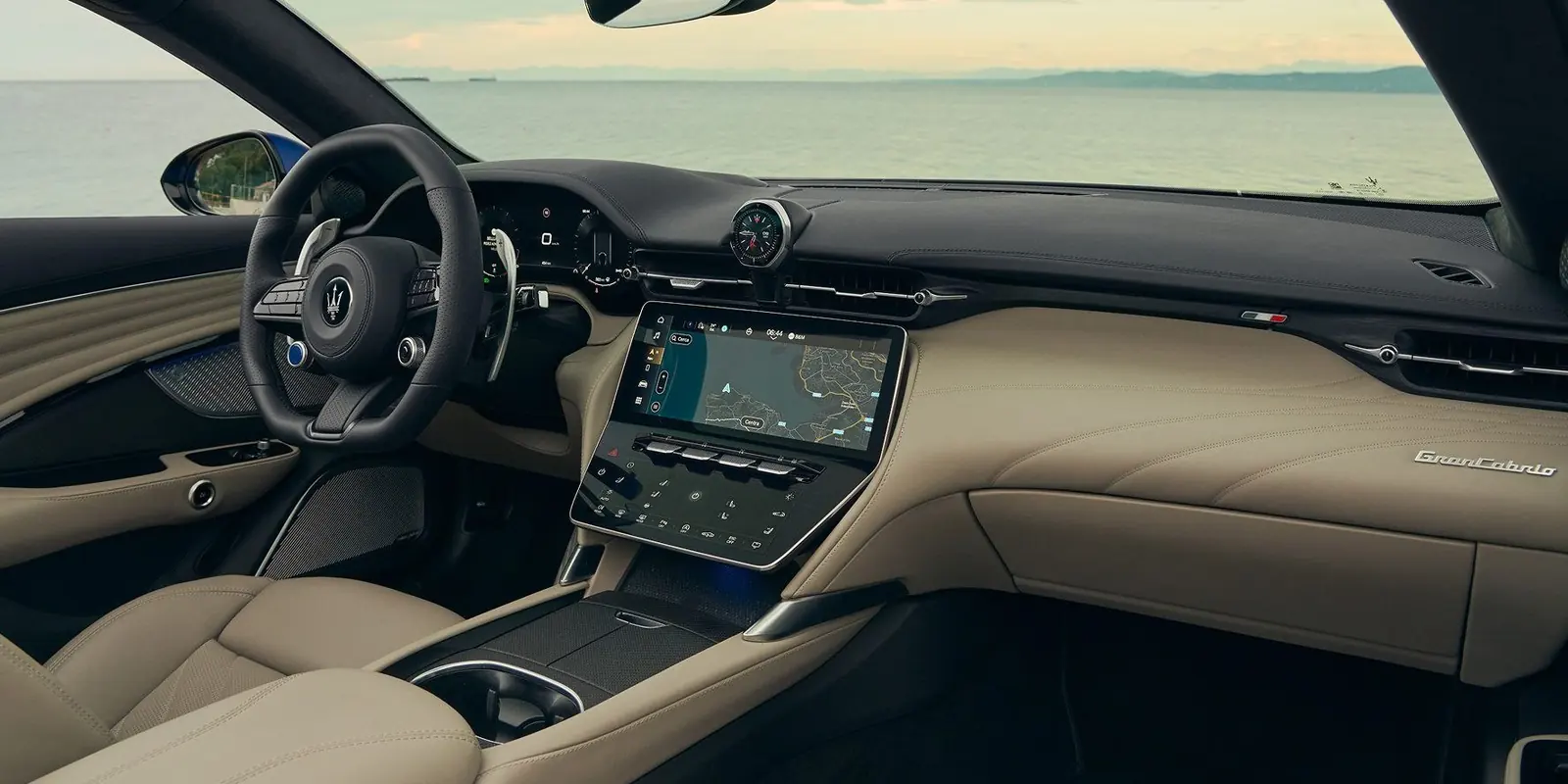 Cockpit des Maserati GranCabrio Modelljahr 2027 mit Lenkrad, Digitaluhr, Zentraldisplay mit Navigationskarte, PRND-Wählschalter und Komfort-Display, Interieur in Beige