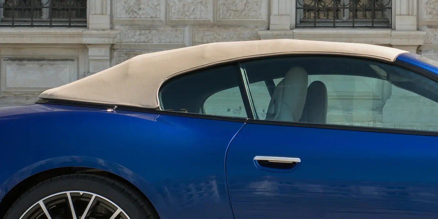 Geschlossenes Stoffverdeck des Maserati GranCabrio Modelljahr 2027 in hellem Beige an einem blauen Fahrzeug vor einer Steinfassade