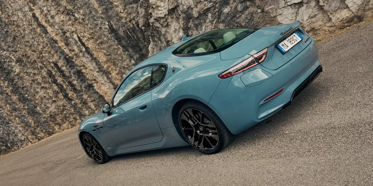 Maserati GranTurismo Folgore Modelljahr 2027 in Hellblau von schräg hinten links auf einer Bergstraße mit Aero-Heckdiffusor und Aura-Aero-Rädern