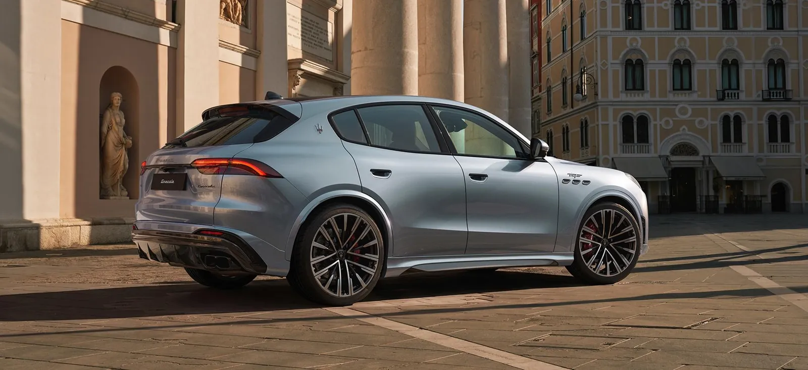 Maserati Grecale Modelljahr 2027 in Hellblau von schräg hinten rechts auf einem Platz vor historischen Fassaden
